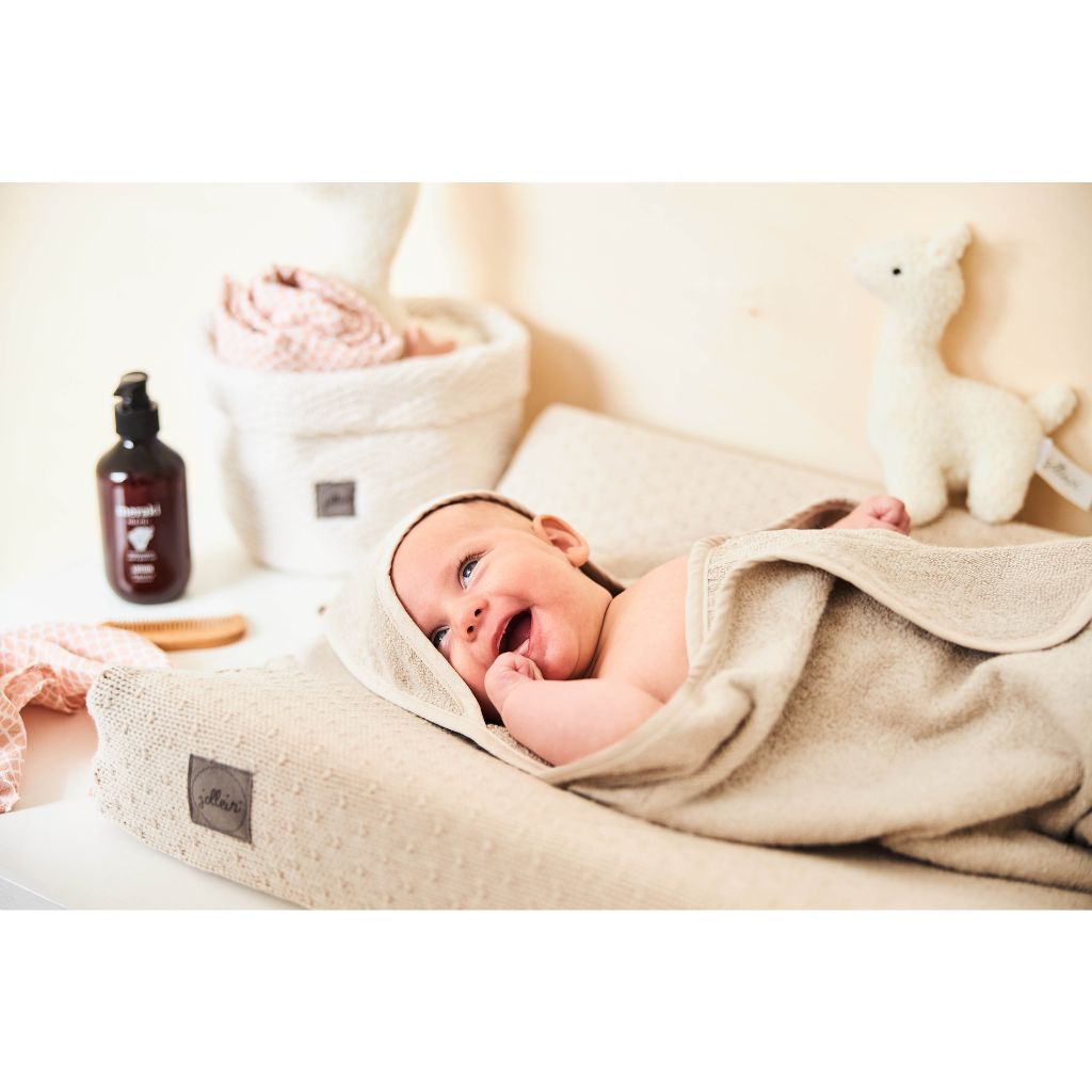 Baby liegt auf Wickelkommode und ist in beiges Kaputzen-Handtuch eingewickelt