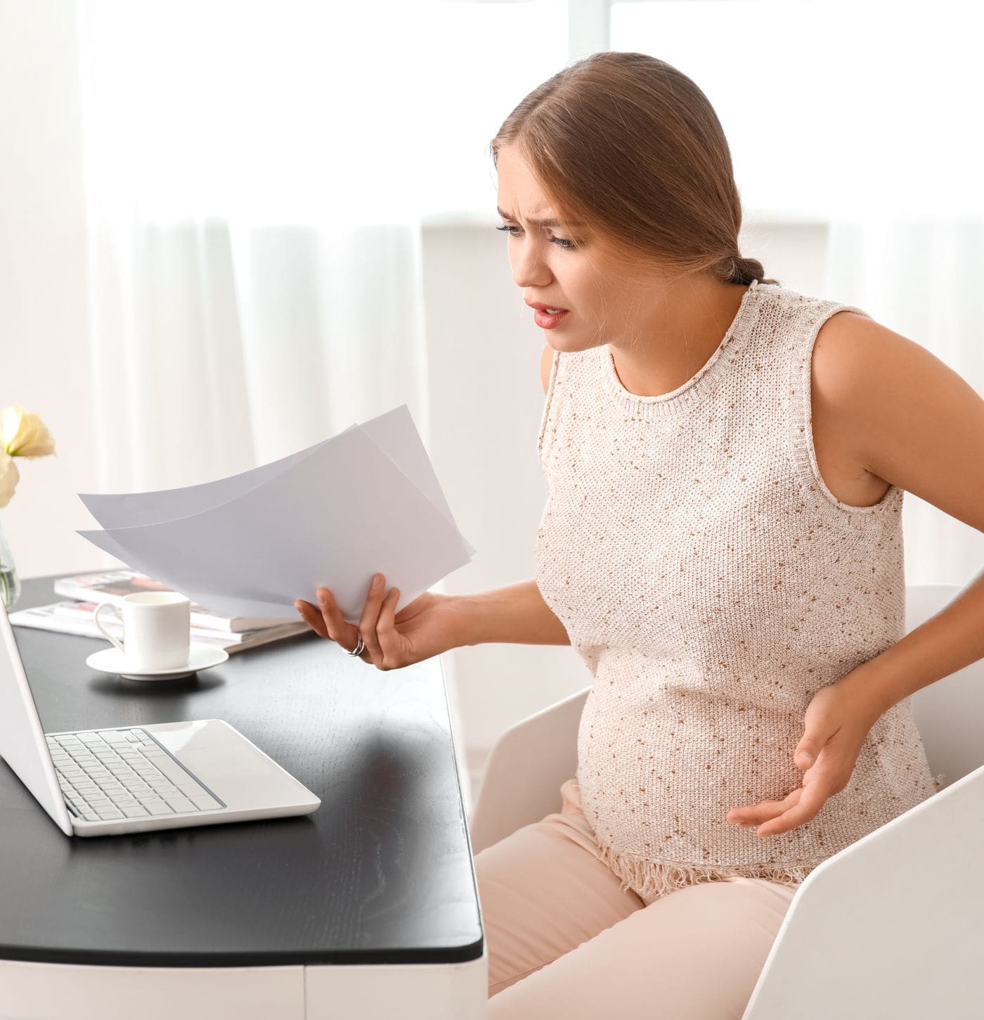 Schwangere Frau mit Formularen am Laptop