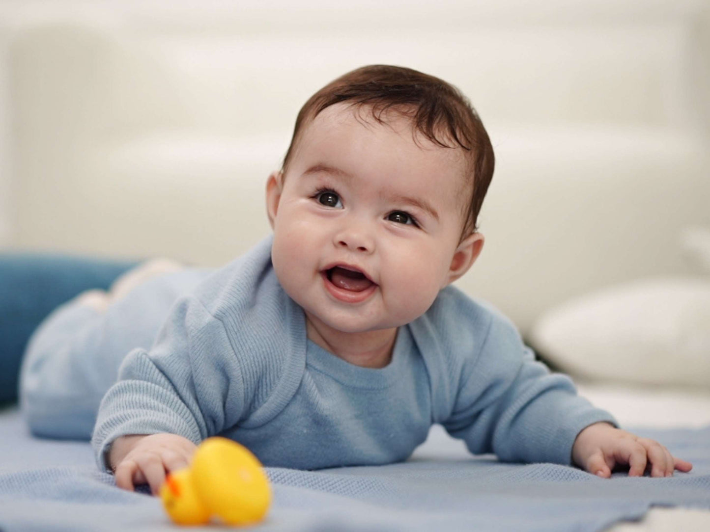 Baby im blauen Strampler aus Merinowolle lacht