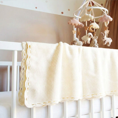 Babydecke in beige hängt über dem Babybettchen