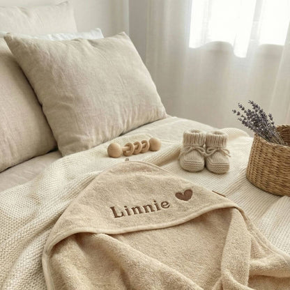 Beiges Baby Kapuzenhandtuch mit Namen und Herz personalisiert liegt ausgebreitet auf dem Bett