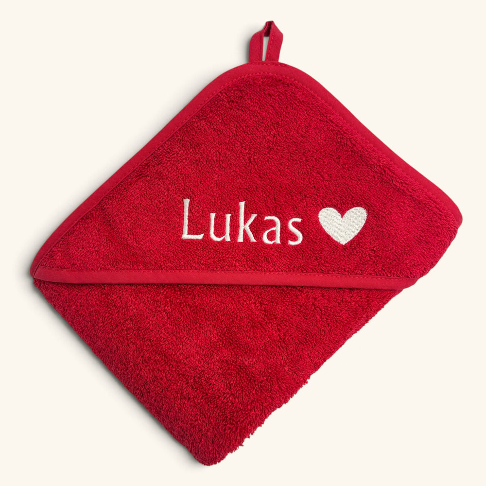 Gefaltetes rotes Kapuzenhandtuch mit Namensstickerei Lukas und Herz in Creme, bestickt in unserem Münchner Atelier