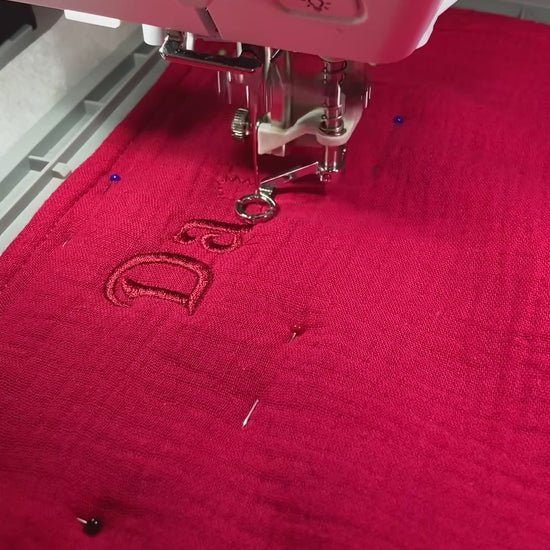 Rotes Geburtstuch wird mit Namen von der Stickmaschine bestickt