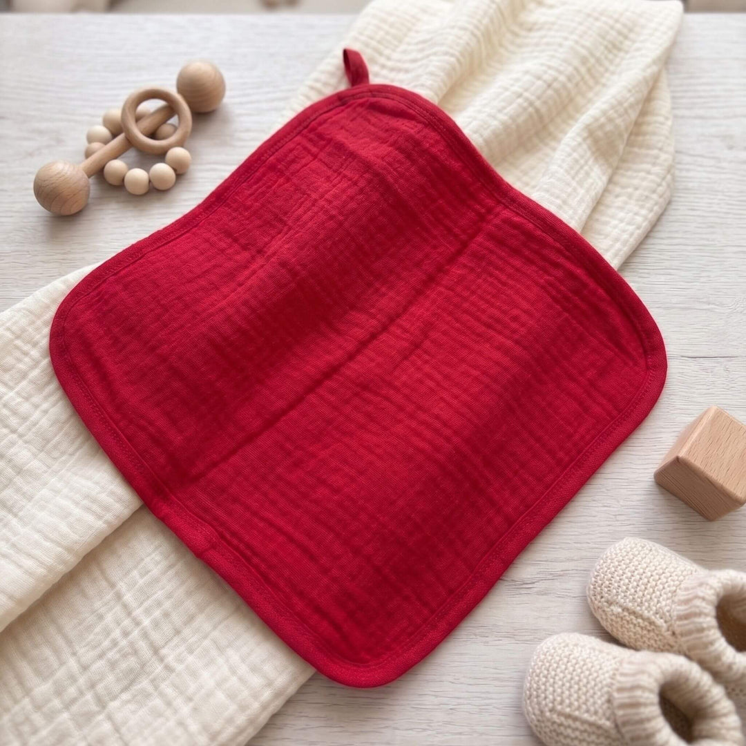 Roter Baby Waschlappen aus Bio-Baumwolle Musselin auf beiger Decke liegend.