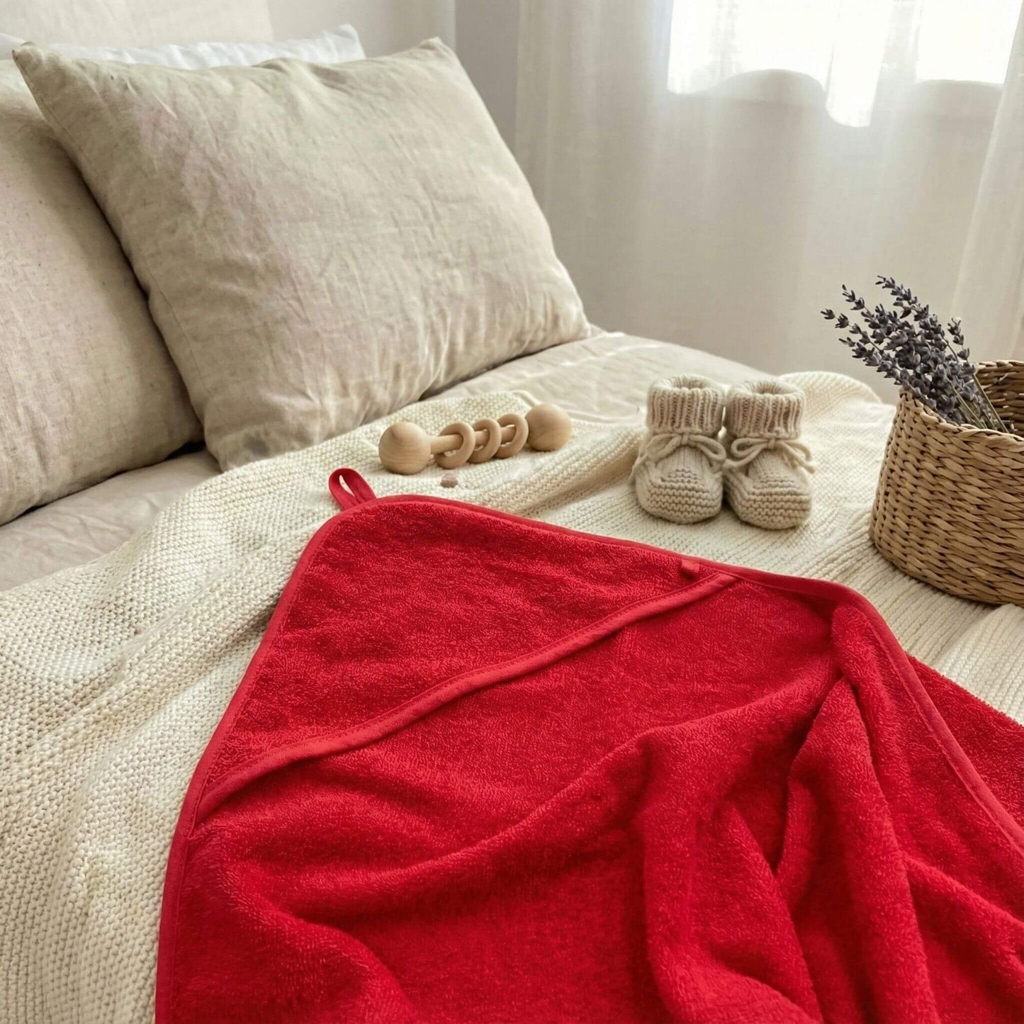 Rotes Baby Kapuzenhandtuch liegt ausgebreitet auf dem Bett neben Babyspielsachen und Wollschuhen