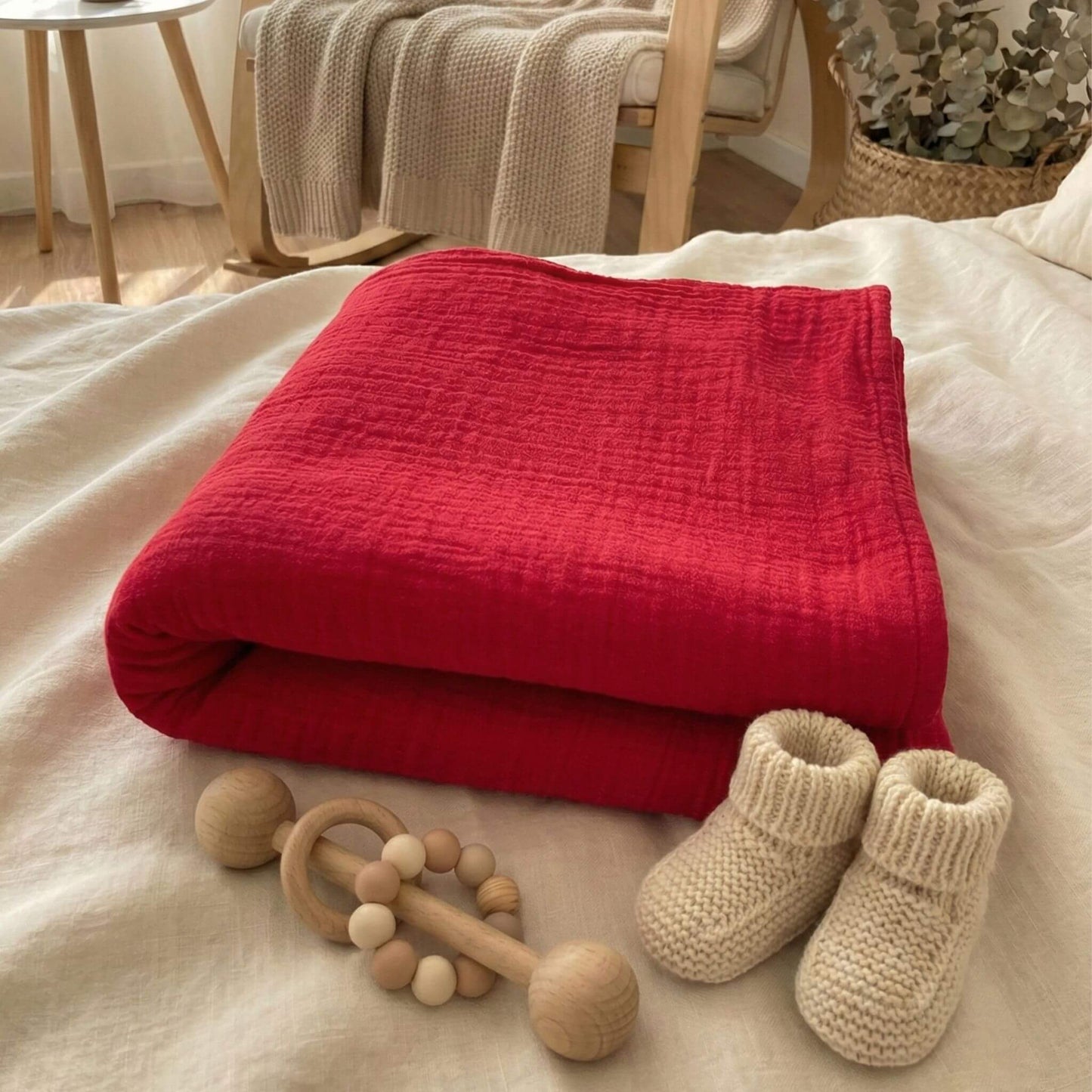 Rotes Geburtstuch liegt zusammengefaltet mit der Musselin-Seite außen auf dem Bett arrangiert und herum liegen ein paar Baby Utensilien