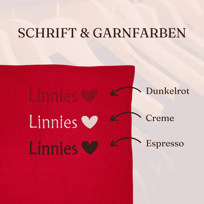 Bild zeigt die beispielhafte Bestickung des Geburtstuchs mit einem Namen und die drei verfügbaren Garnfarben (Dunkelrot, Creme / Weiß / Espresso Braun)