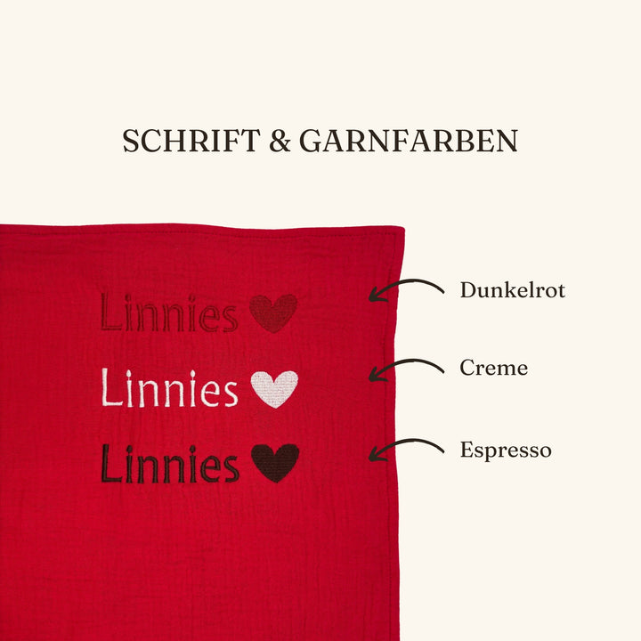 Bild zeigt die beispielhafte Bestickung des Geburtstuchs mit einem Namen und die drei verfügbaren Garnfarben (Dunkelrot, Creme Weiß / Espresso Braun)