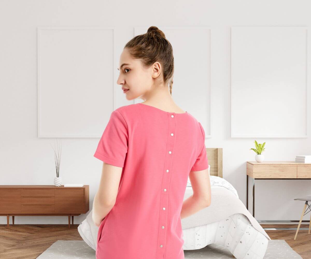 Schwangere trägt Geburtskleid und zeigt den Rücken mit der Knopfleiste die im Falle eine PDA aufgeknöpft werden kann